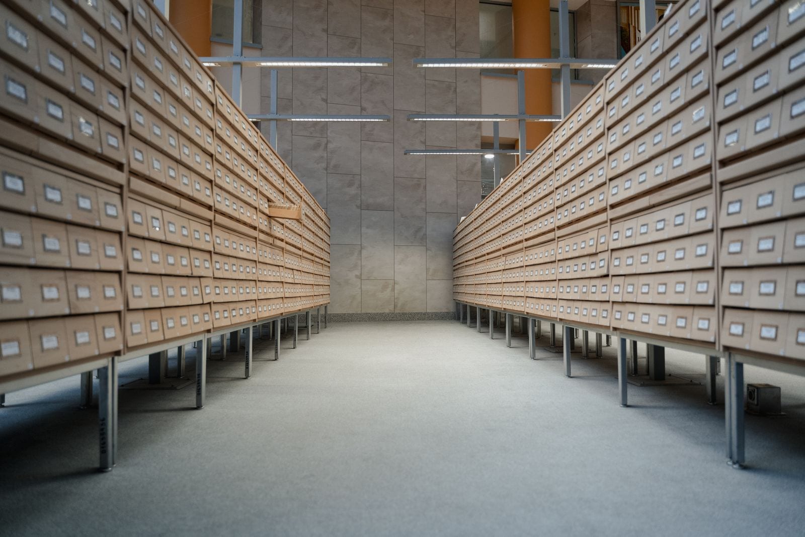 Two facing runs of wooden card-catalogue drawers receding down an archive aisle