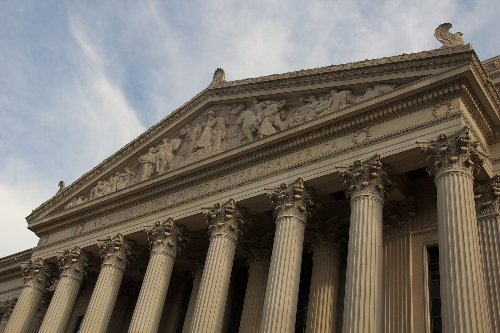 The columned portico of the National Archives building in Washington, DC, seen from below, with ARCHIVES OF THE UNITED STATES OF AMERICA carved across the frieze