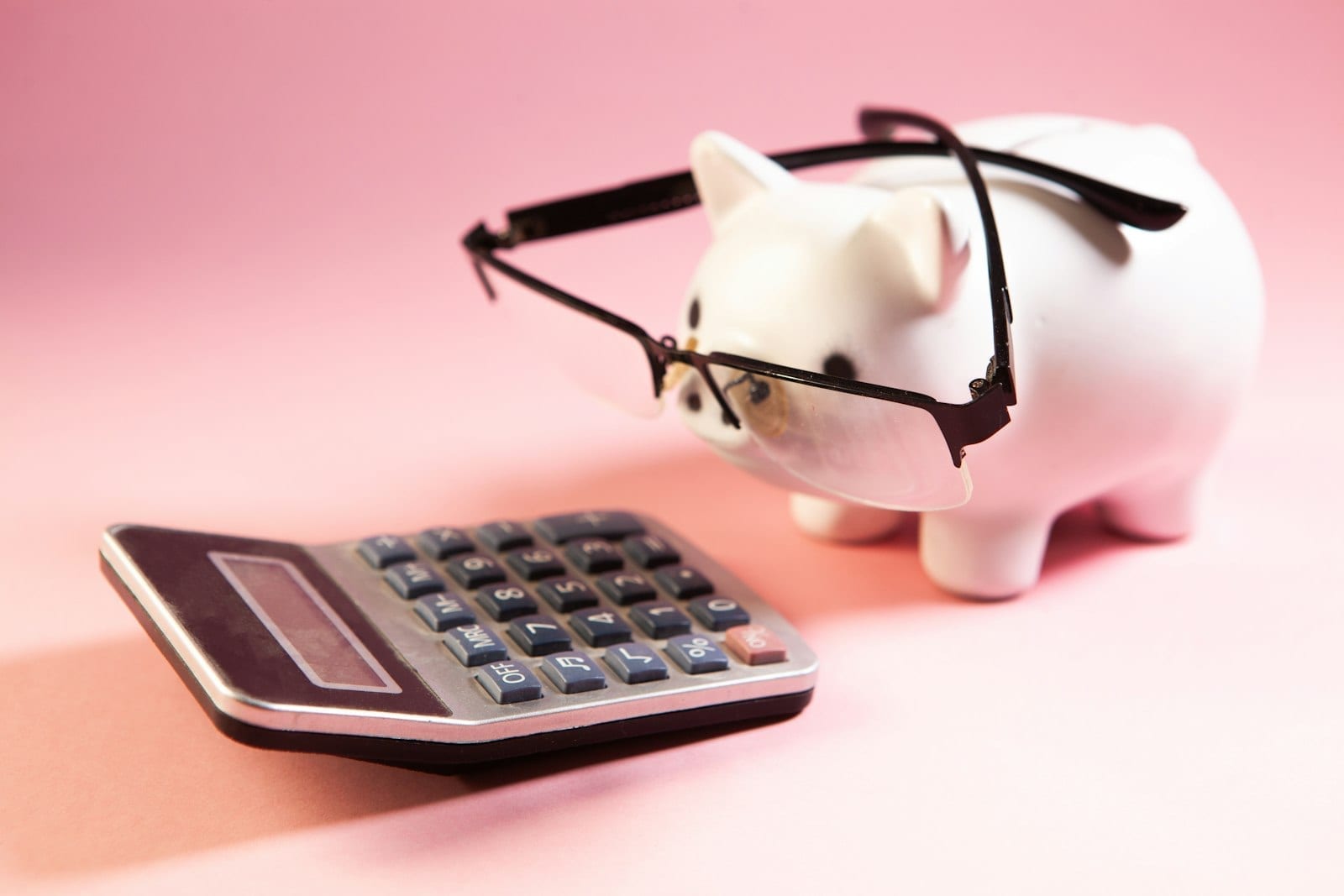 A pink piggy bank wearing glasses next to a calculator