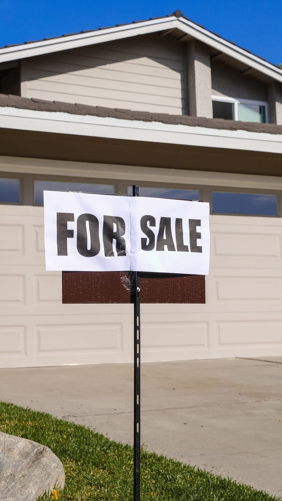 A modern suburban house with a prominent For Sale sign in the front yard