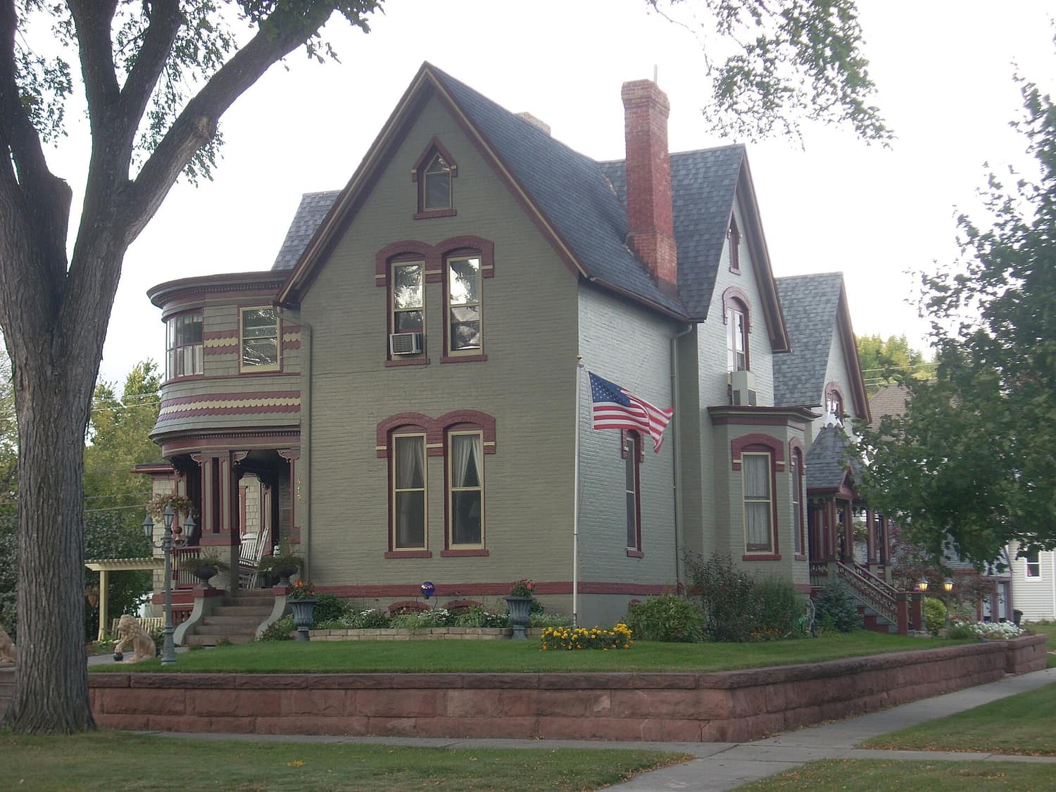 A brick Gothic-Italianate Victorian house with a steep gabled roof on a residential street in Grand Forks, North Dakota